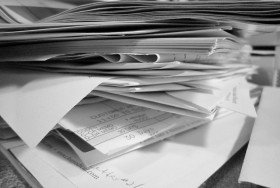 A messy stack of papers on a desk, which can be avoided by digitalizing all paperwork via data management software.