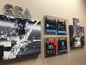 One of the walls at the Shop Floor Automations office, which displays two machine-related canvas prints and various SFA mousepads from over the years.