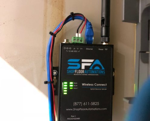 A 1-Port Wireless Connect unit powered on with its antenna directly attached. The unit is mounted to the wall and has one serial cable connected.