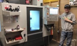 Payton, an 18 year old machinist, standing next to his Haas DM2 CNC machine.