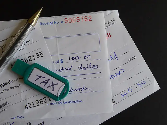 A green USB drive with the word "Tax" on it sits on top of a pile of tax payment checks.