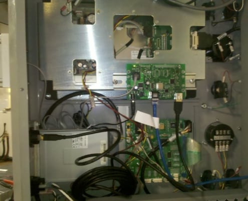 The inside of a CNC machine controller, showing the USB Connect Pendant connected to the circuit board via serial cable.