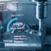A close up of a CNC machine tool head at work carving metal. There is text overlaid, showing various machine stats such as speed and blocktype.